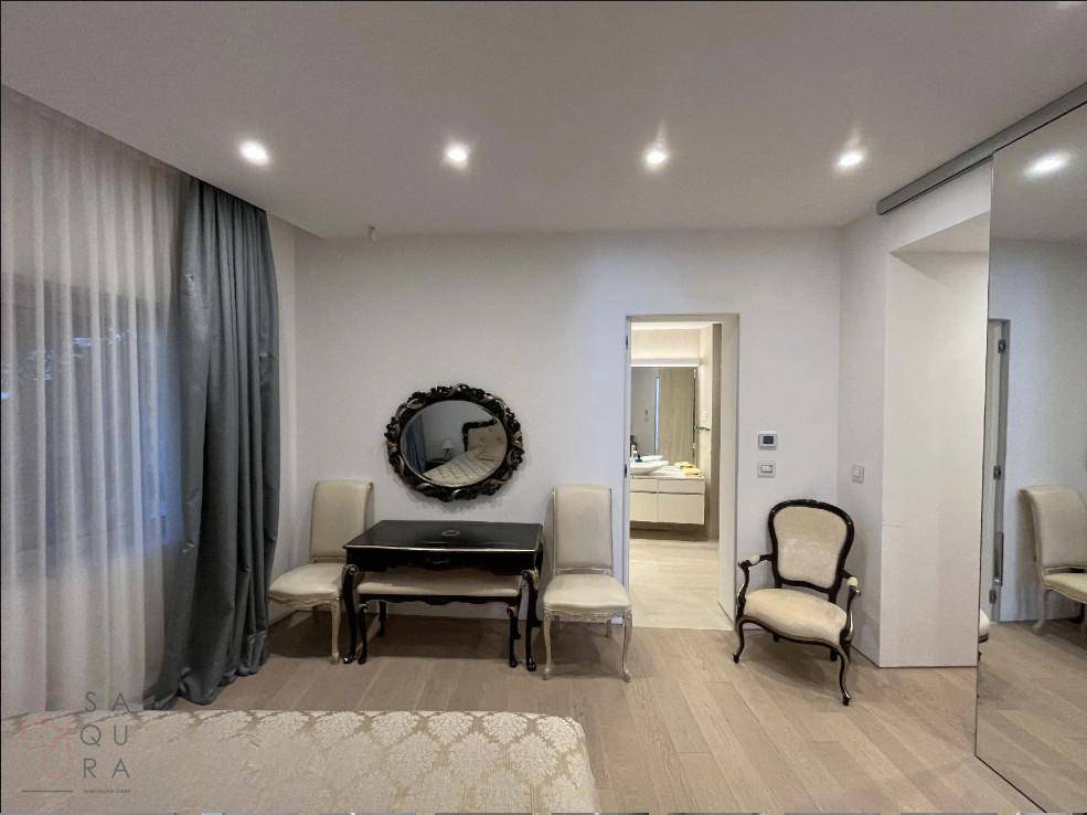 Helles Schlafzimmer mit klassischem Mobiliar, großem Fenster und Zugang zum Badezimmer.