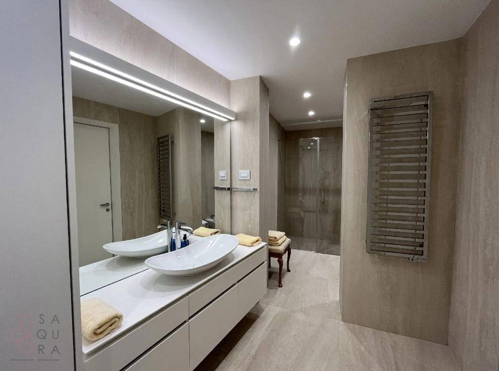 Helles Badezimmer mit Doppelwaschbecken, beheiztem Handtuchhalter und begehbarer Dusche.