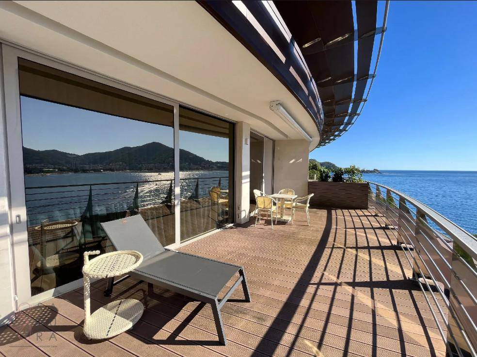 Geräumige Terrasse mit Holzboden, Liegestuhl und weitem Blick über die Küste und das Meer.