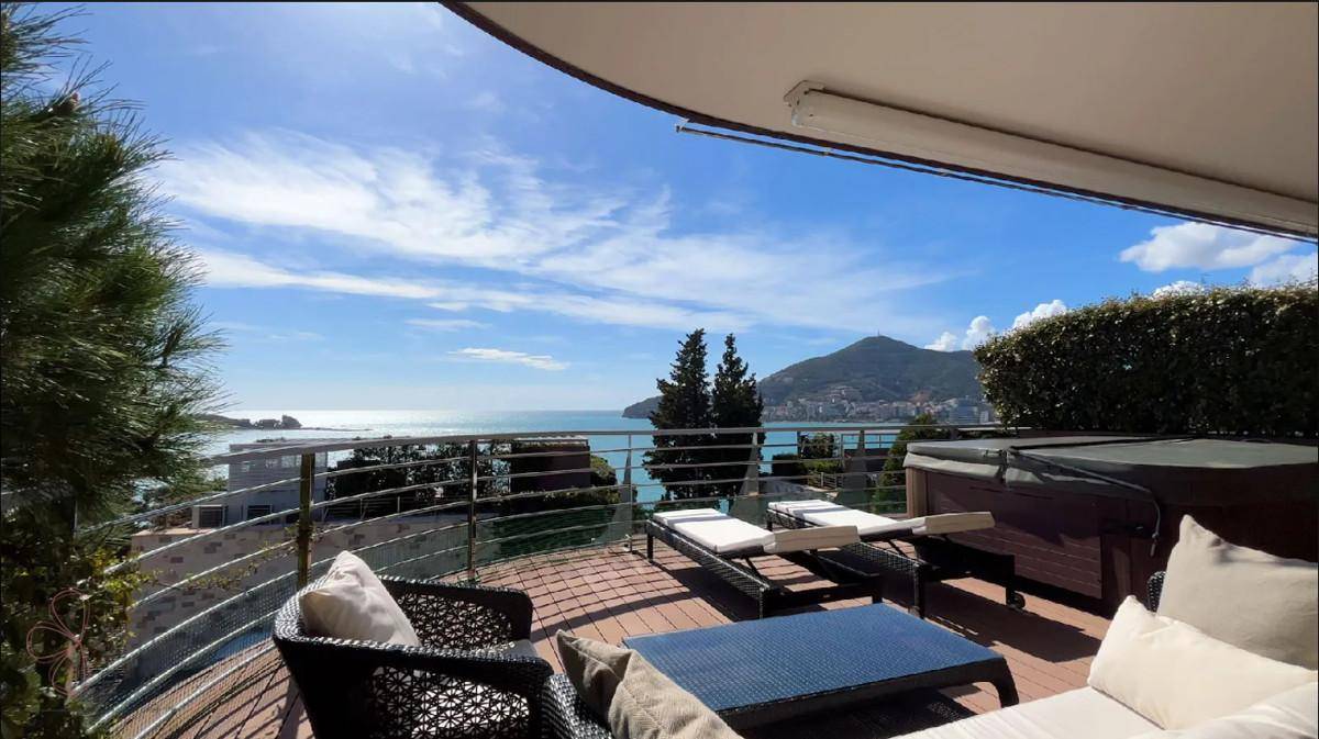 Große Terrasse mit Meerblick, Sonnenliegen und Whirlpool unter blauem Himmel.