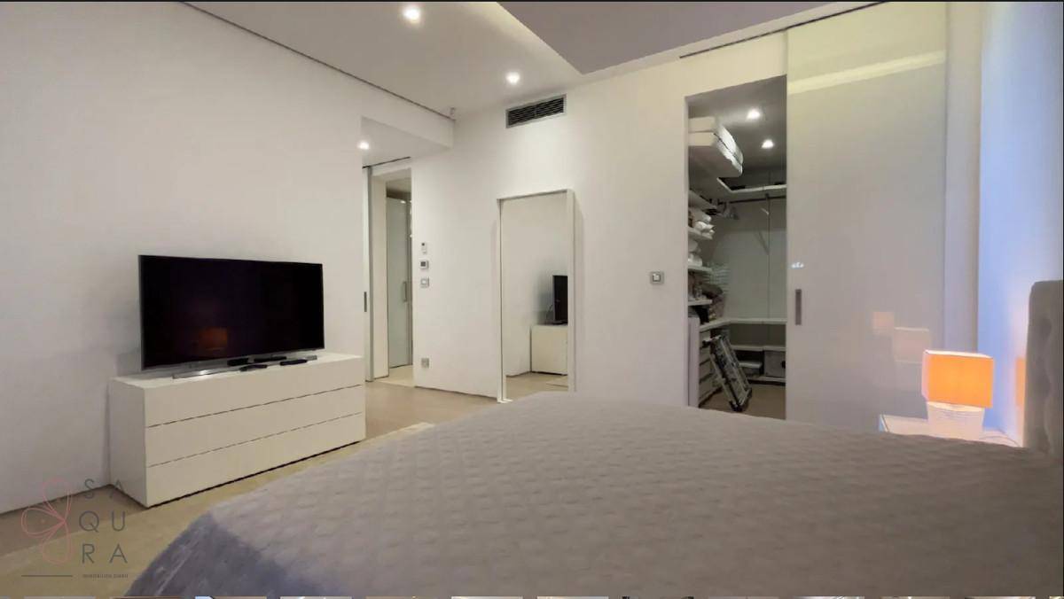 Helles Schlafzimmer mit modernem Bett, Fernseher und Zugang zu einem begehbaren Kleiderschrank.