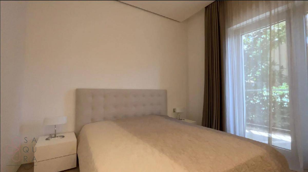 Gemütliches Schlafzimmer mit einem bequemen Bett, Nachttisch und großem Fenster mit Vorhängen.