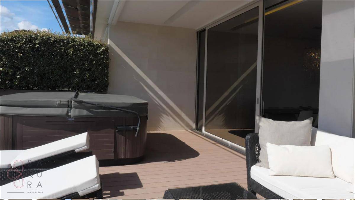 Sonniger Terrassenbereich mit Whirlpool, Sitzgelegenheiten und Schiebetüren zum Innenbereich.