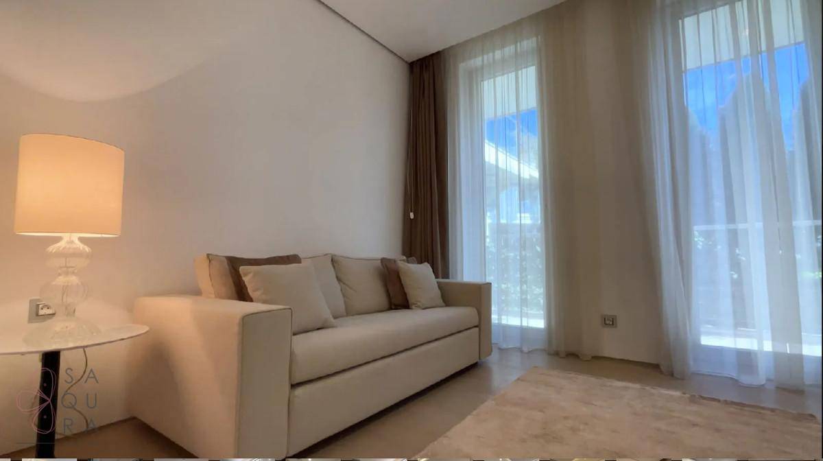 Helles Wohnzimmer mit bequemem Sofa, Stehlampe und großen Fenstern mit Vorhängen.