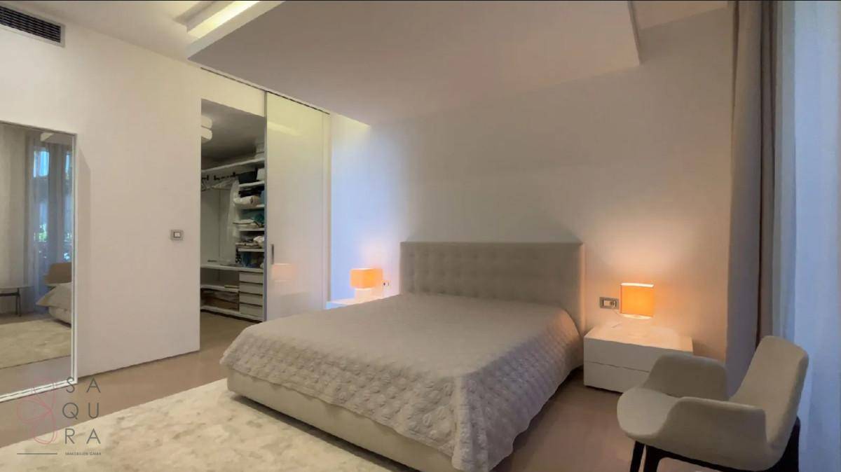 Modernes Schlafzimmer mit hellem Bett, Nachttischlampen und Zugang zu einem begehbaren Kleiderschrank.