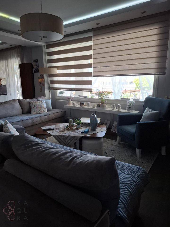 Wohnzimmer mit bequemen Sofas, einem Sessel und einem Fenster mit gestreiften Rollos.