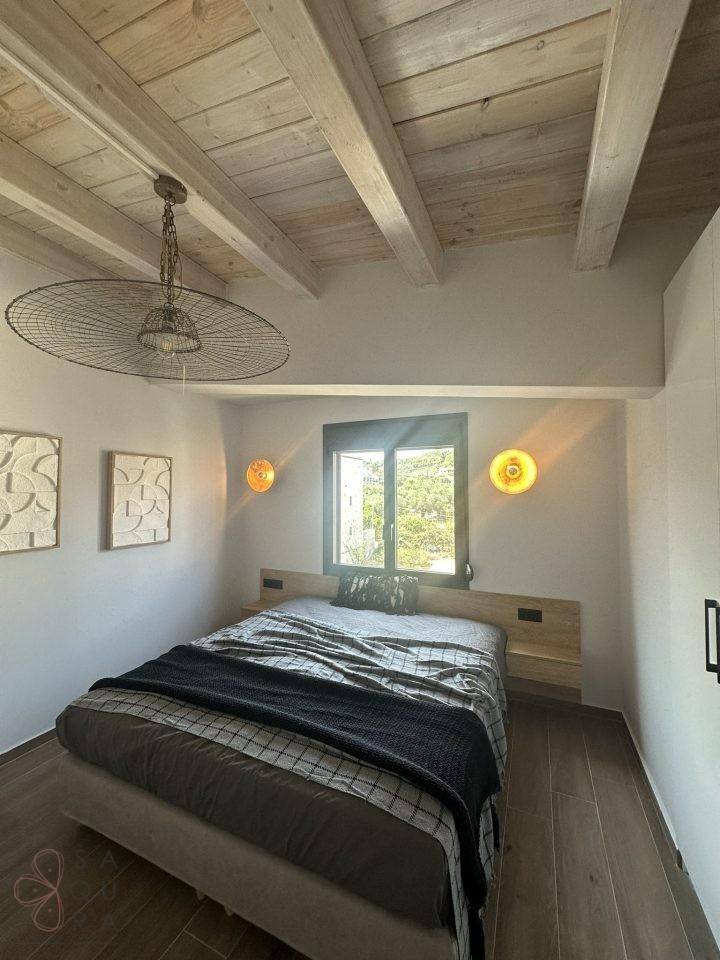 Schlafzimmer mit Holzbalkendecke, modernem Bett und Blick ins Grüne.
