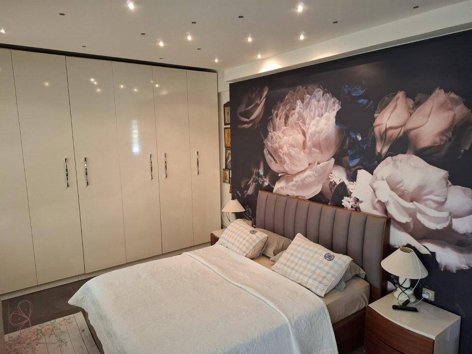 Elegantes Schlafzimmer mit Doppelbett, glänzenden Einbauschränken und auffälliger Blumentapete.