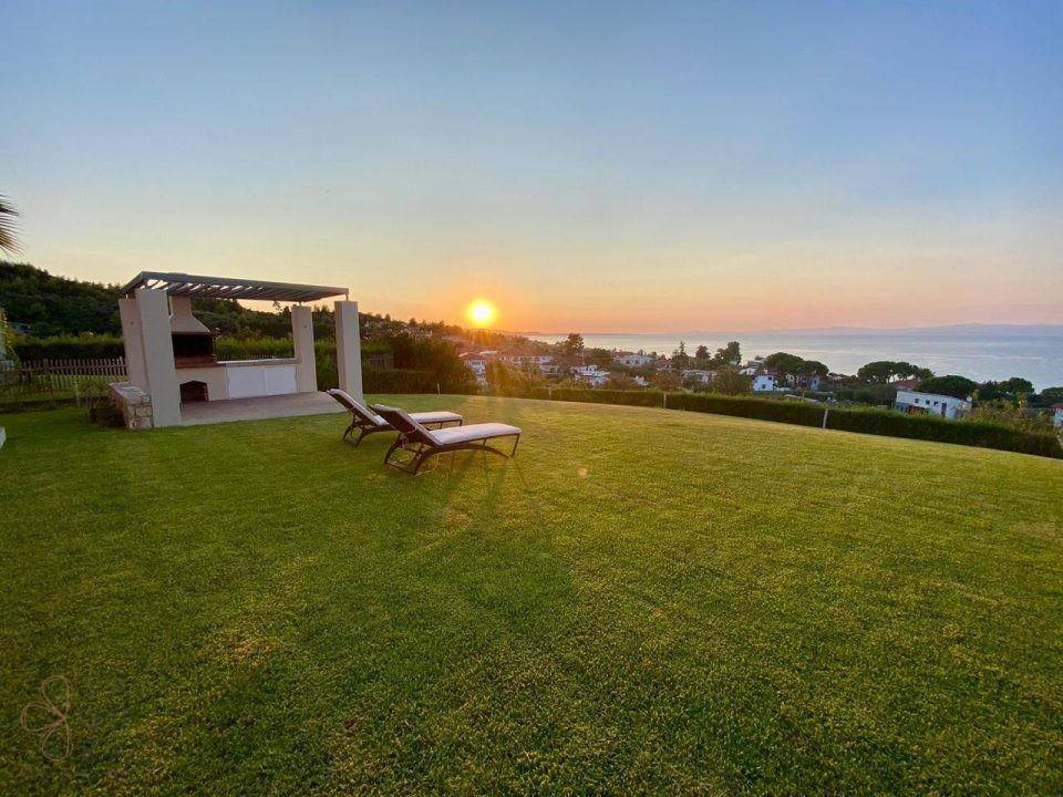 Malerischer Sonnenuntergang über dem Meer, sichtbar vom weitläufigen Garten mit Grillbereich.