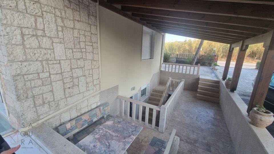 Überdachte Außenterrasse mit Sitzgelegenheiten, Steinfliesen und Treppen.