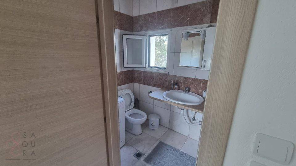Badezimmer mit WC, Waschbecken, Fenster und braun-weißen Fliesen.