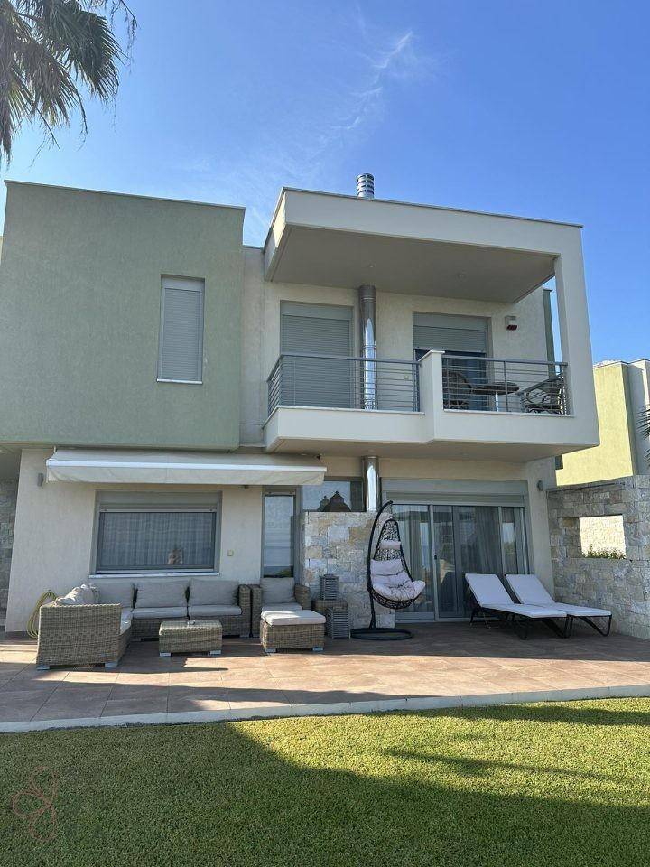 Elegante Villa mit großer Terrasse, Rasenfläche und bequemen Sonnenliegen im Freien.