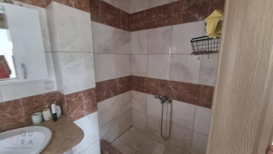 Badezimmer mit Duschbereich, Waschbecken und braun-weißen Fliesen.