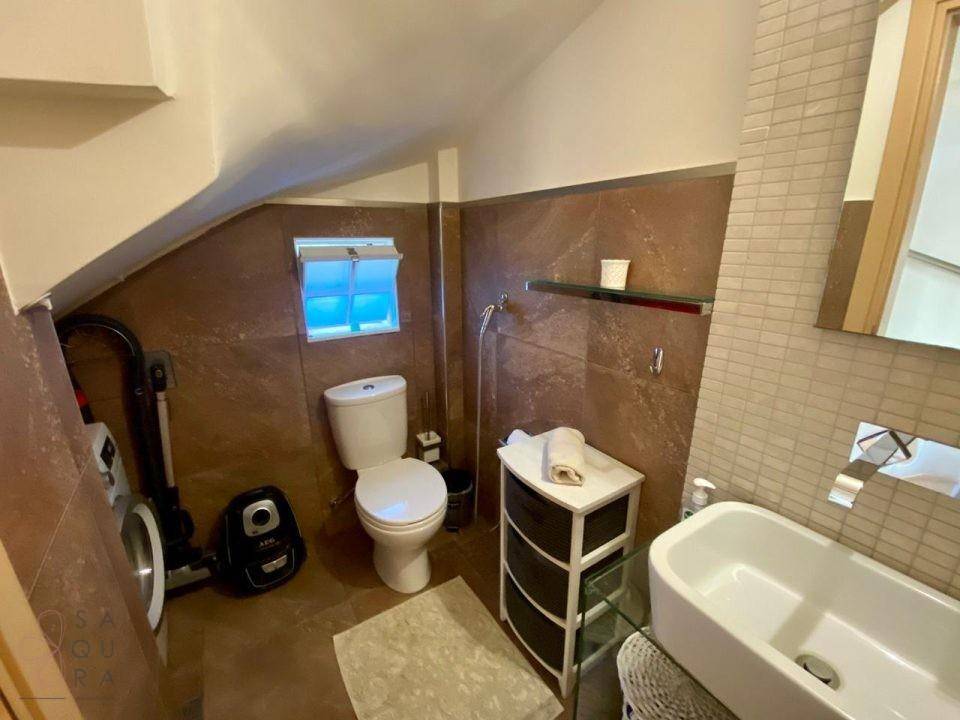 Badezimmer im Dachgeschoss mit Schräge, WC und Waschbecken, das auch eine Waschmaschine beherbergt.