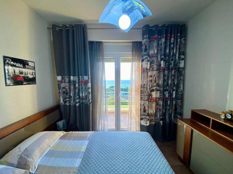 Schlafzimmer mit Doppelbett, Balkonzugang und Vorhängen mit Stadtmotiv, die einen Meerblick ermöglichen.