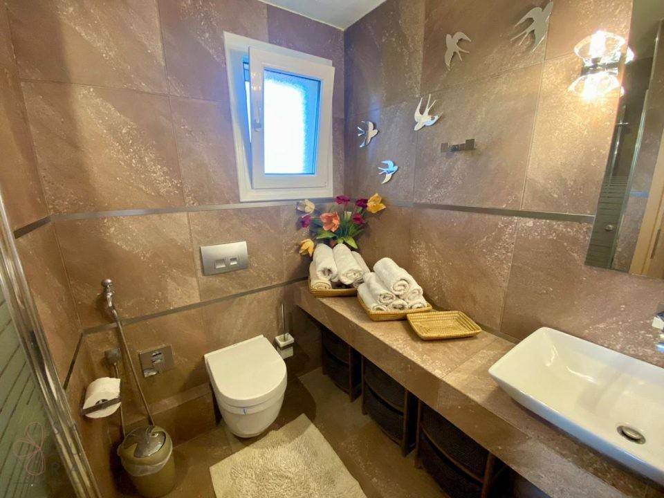 Modernes Badezimmer mit braunen Fliesen, wandmontiertem WC und einem stilvollen Aufsatzwaschbecken.