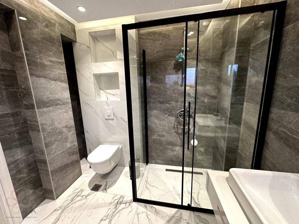 Stilvolles Badezimmer mit dunklen Wandfliesen, wandhängendem WC und geräumiger Duschkabine.