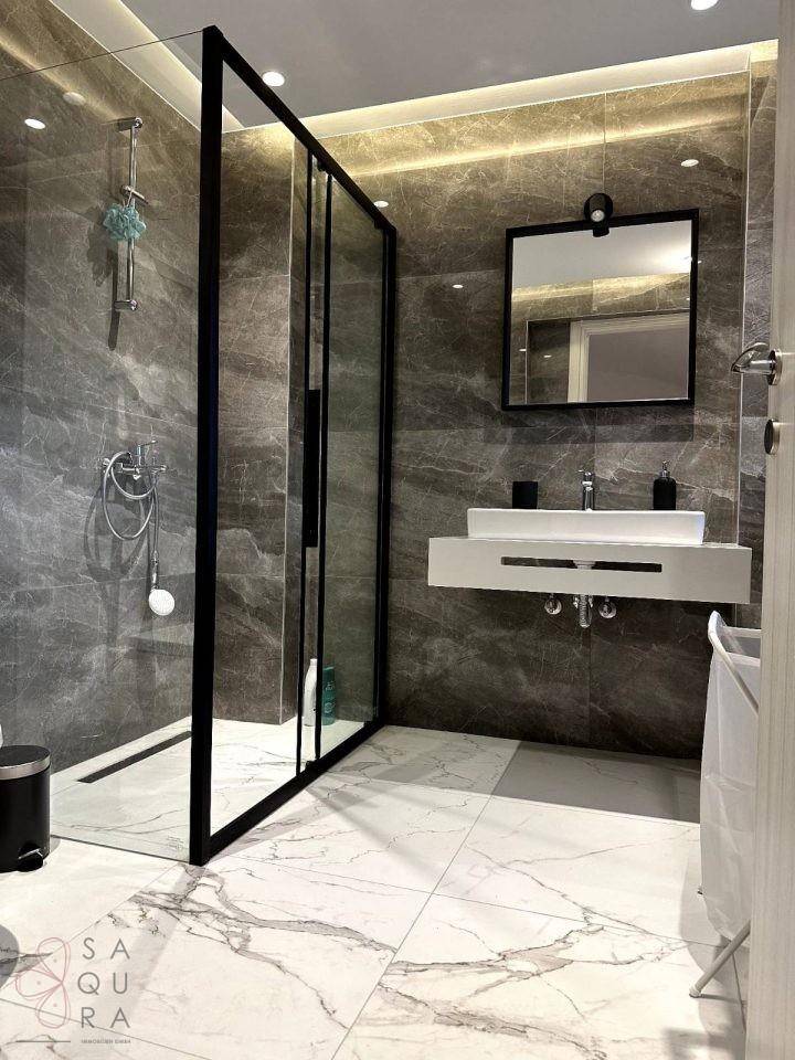 Elegantes Badezimmer mit dunklen Wandfliesen, Glasduschkabine und modernem Waschtisch.