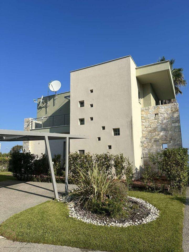Zeitgenössische Villa mit Carport und minimalistischer Fassade, umgeben von mediterraner Vegetation.