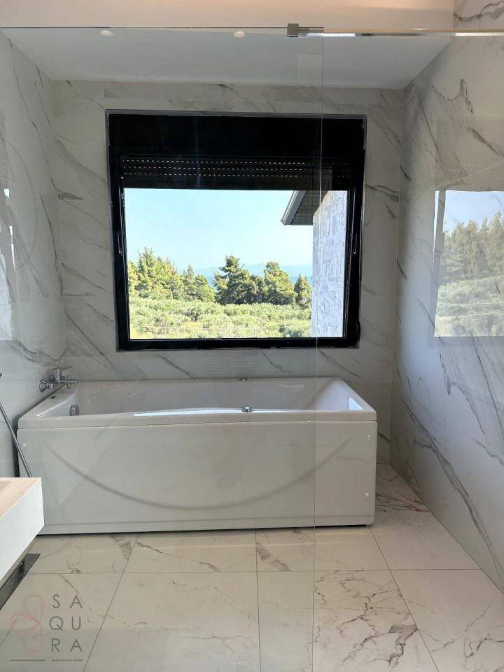 Helles Badezimmer mit Badewanne, großen Marmorfliesen und Fenster mit Blick ins Grüne.