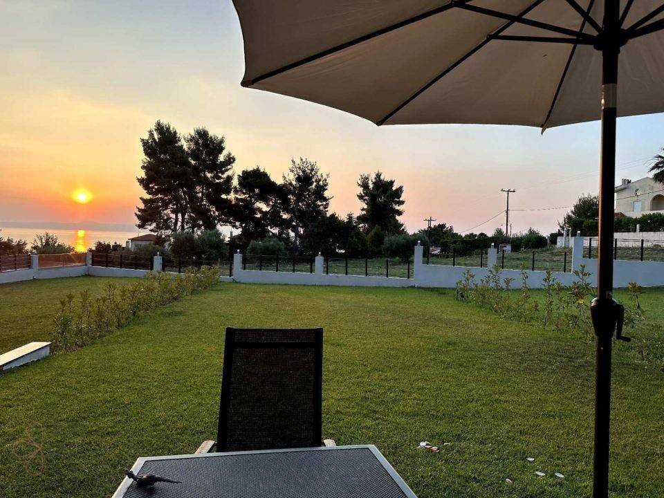 Gepflegter Gartenbereich mit Rasenfläche und Meerblick bei Sonnenuntergang, ideal zum Entspannen.