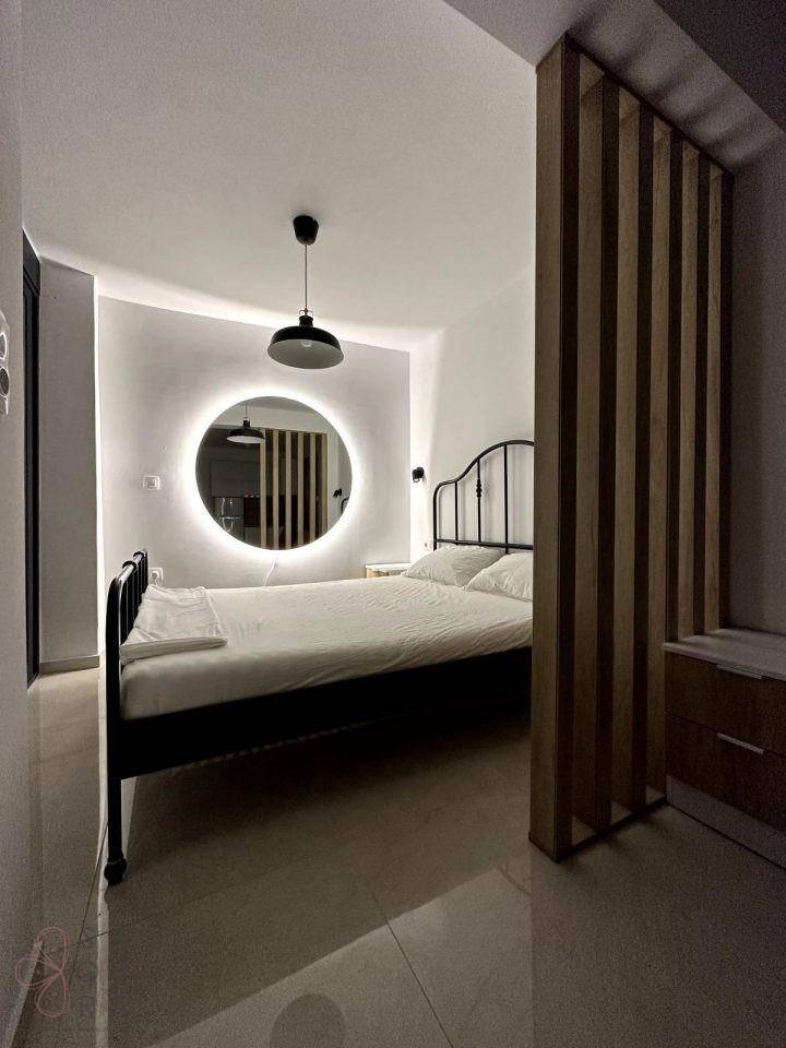 Gemütliches Schlafzimmer mit Doppelbett, beleuchtetem Rundspiegel und Holztrennwand, modern eingerichtet.