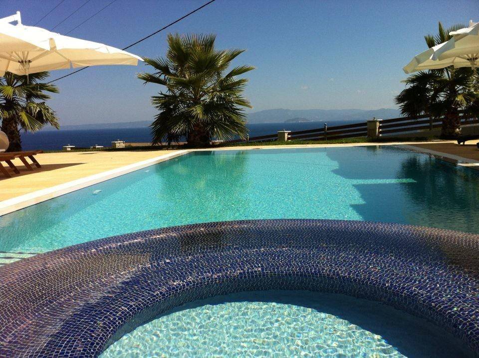 Großer Pool mit integriertem Whirlpool und weitem Meerblick unter strahlend blauem Himmel.