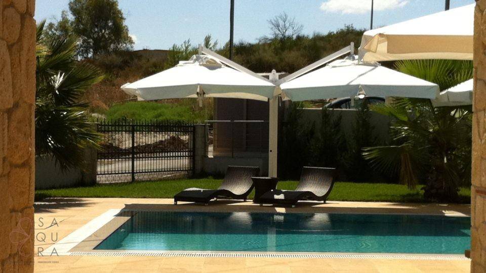 Poolbereich mit bequemen Sonnenliegen, großen Sonnenschirmen und umzäuntem Garten.