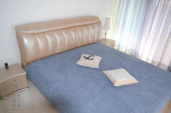 Schlafzimmer mit beigem Lederbett, blauer Tagesdecke und Nachttischen.