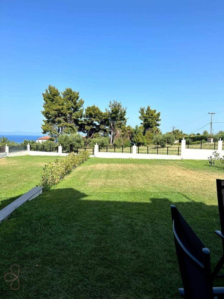 Weitläufiger Garten mit Rasenfläche und Blick auf das Meer unter blauem Himmel.