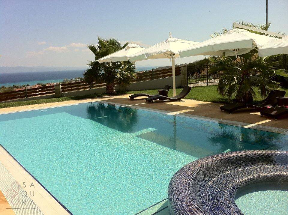 Entspannender Poolbereich mit Meerblick, Sonnenliegen und Palmen unter blauem Himmel.