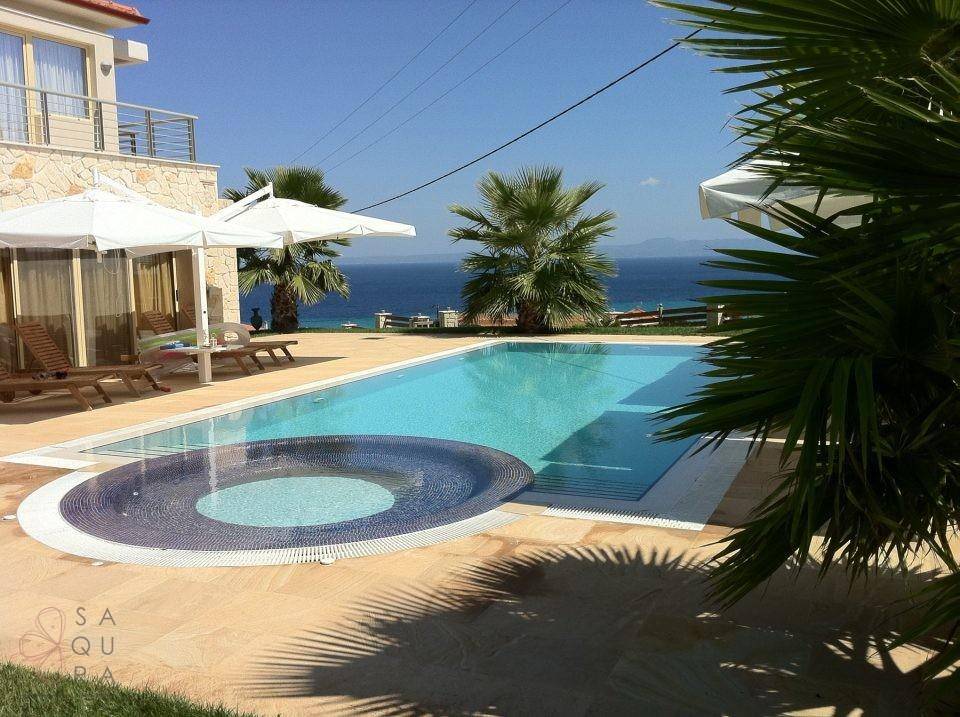 Luxuriöser Poolbereich mit Meerblick, Sonnenliegen und Palmen unter blauem Himmel.