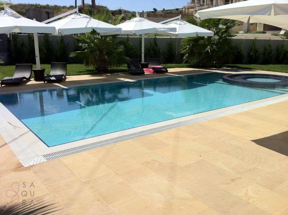 Weitläufiger Poolbereich mit Sonnenliegen, großen Sonnenschirmen und gepflegtem Rasen.