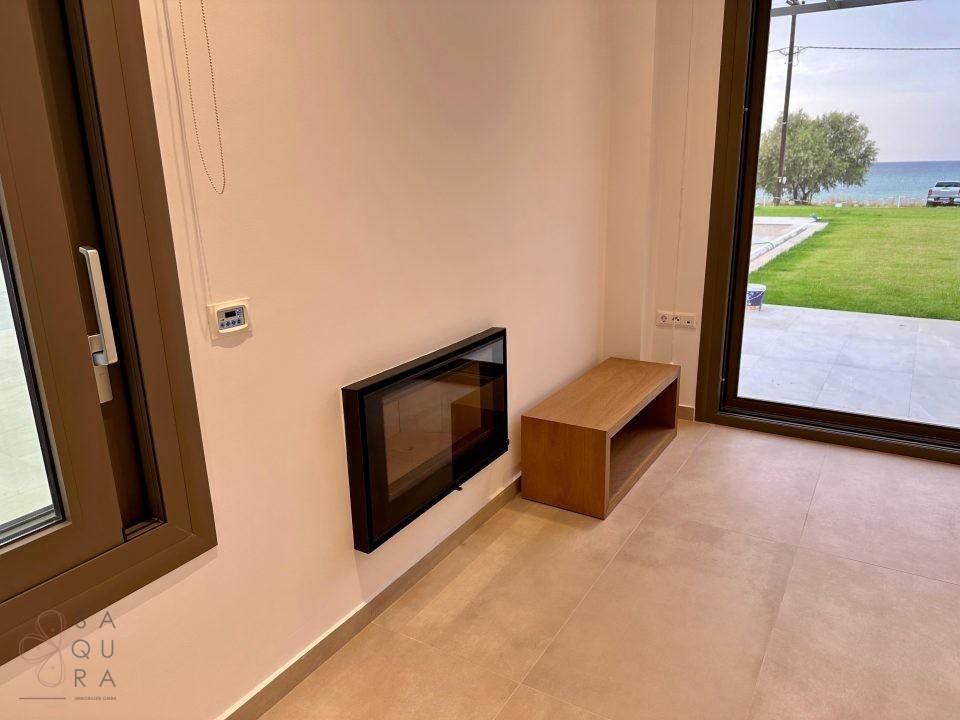 Moderner Wandkamin in einem hellen Raum mit großen Fenstern und Blick ins Grüne.