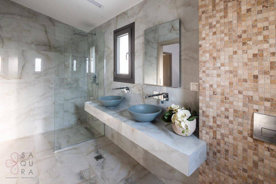 Luxuriöses Badezimmer mit zwei Waschbecken, großer Dusche und dekorativen Mosaikfliesen.