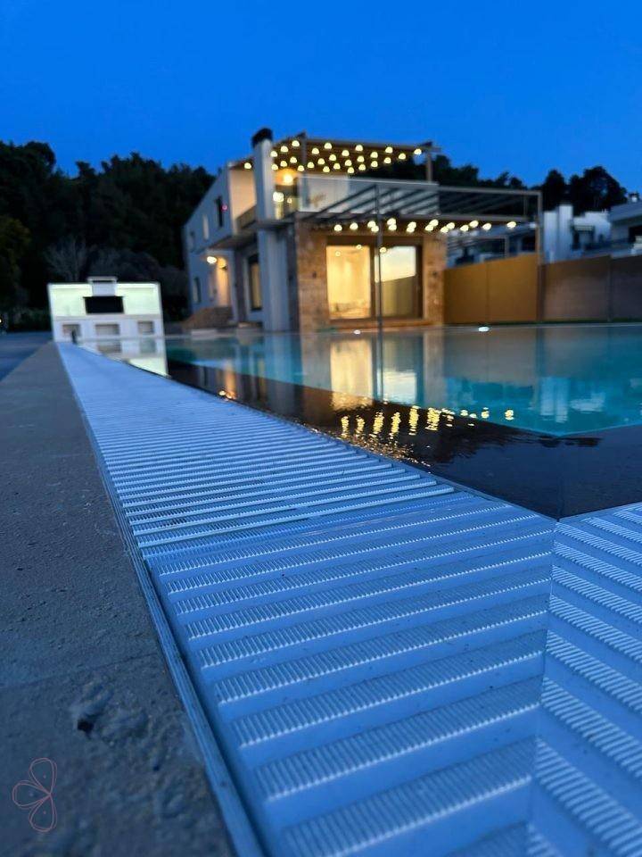Nahaufnahme des Pools mit reflektierendem Licht und der modernen Villa im Hintergrund bei Nacht.
