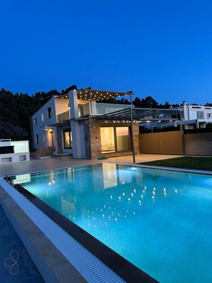 Elegante Villa mit großem, beleuchtetem Pool und Pergola unter dem Nachthimmel.