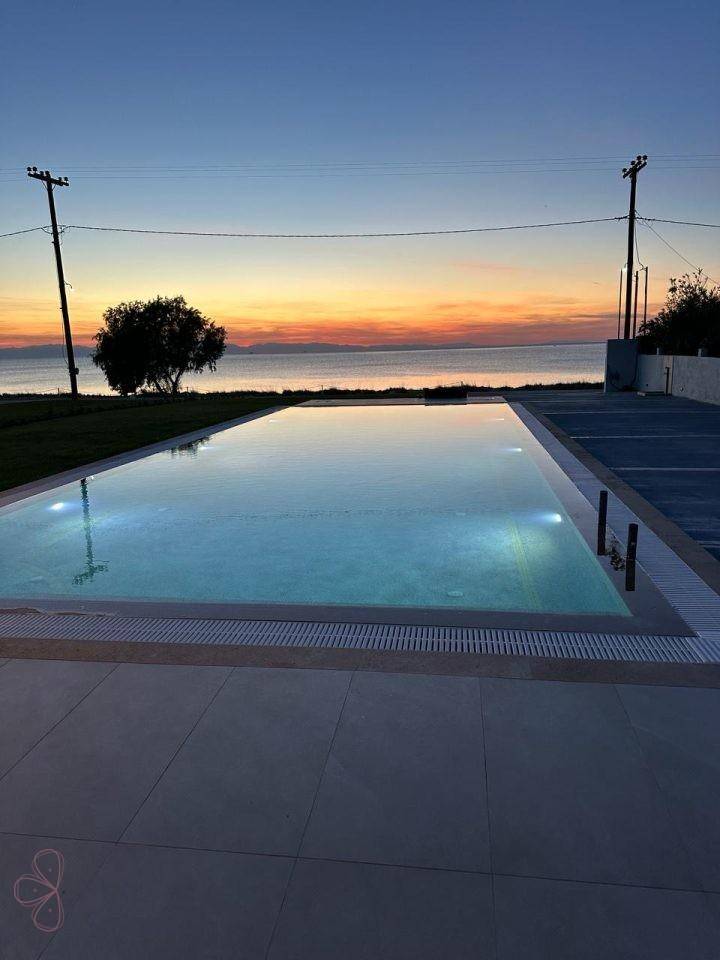 Langer, schimmernder Pool mit direktem Meerblick und einem malerischen Sonnenuntergang.