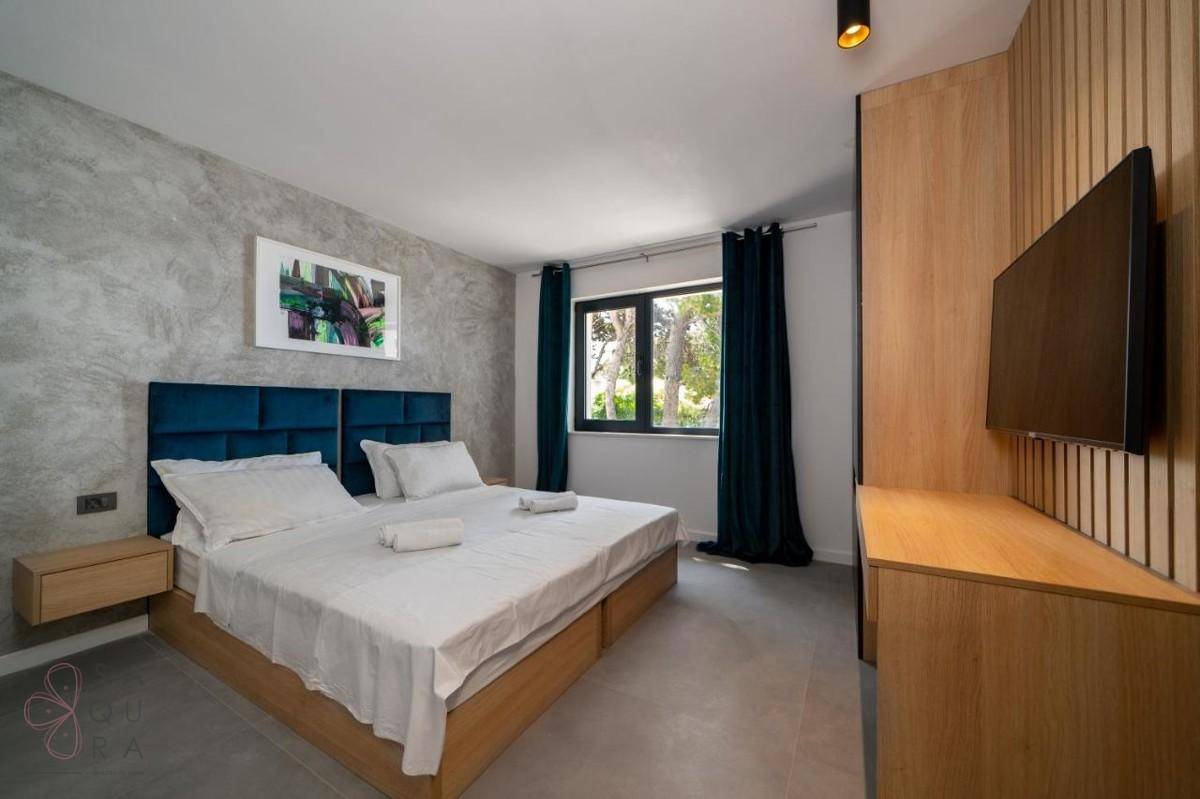 Helles Schlafzimmer mit Doppelbett, Holzakzenten und einem an der Wand montierten Fernseher.