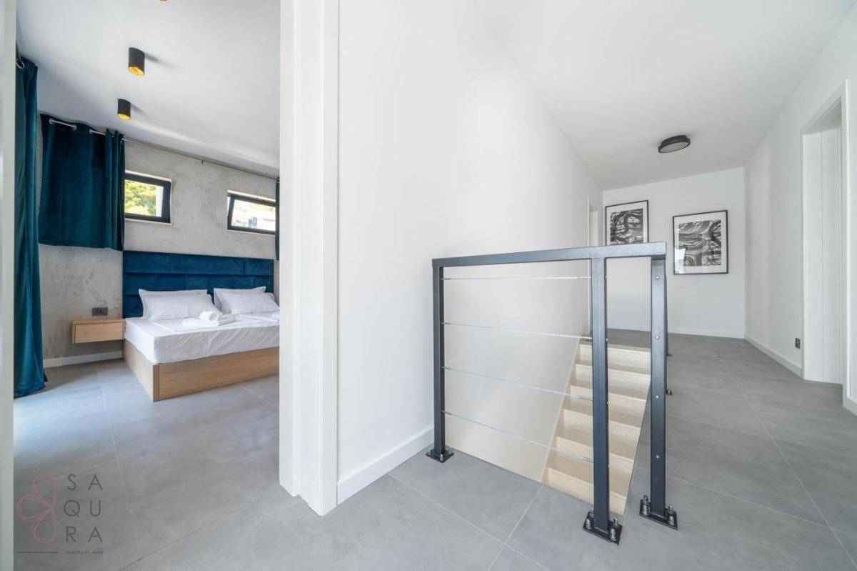 Flur mit Treppenabgang und Blick in ein modern eingerichtetes Schlafzimmer.
