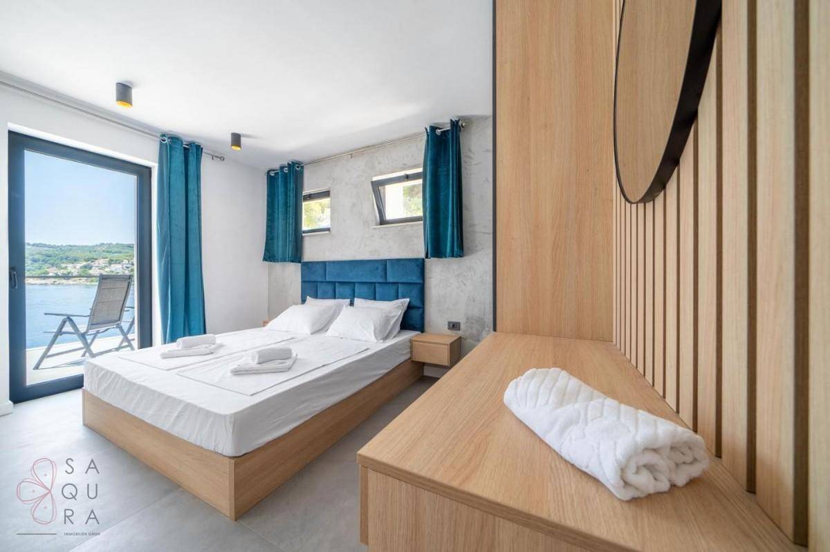 Schlafzimmer mit Doppelbett, Holzakzenten und direktem Zugang zu einem Balkon mit Meerblick.