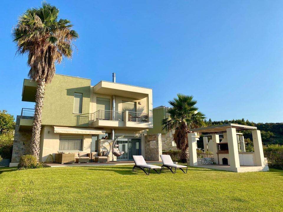 Moderne Villa mit großem Garten, Terrasse und Grillplatz, umgeben von Palmen und Meerblick.