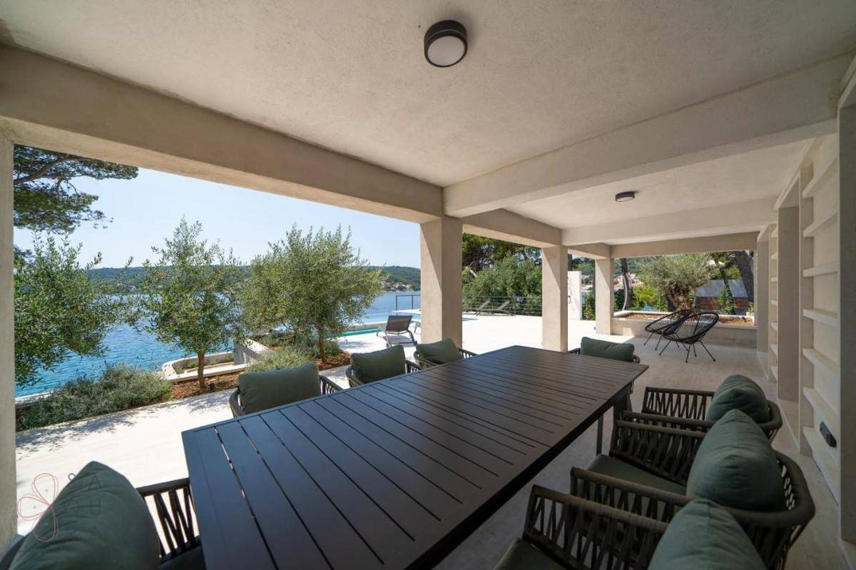Überdachter Essbereich im Freien mit großem Tisch und Stühlen, ideal für Mahlzeiten mit Meerblick.