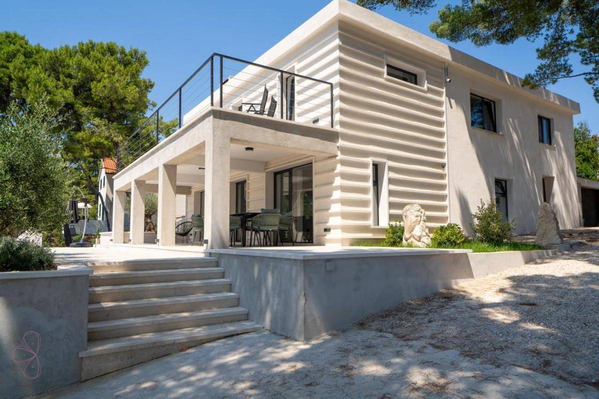 Moderne Villa mit gestufter Architektur und Außentreppe, umgeben von mediterraner Vegetation.
