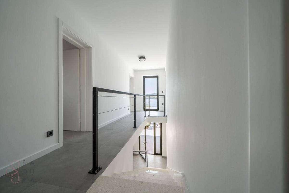 Heller Flur mit moderner Treppe und Blick auf das Meer durch die Glastür.