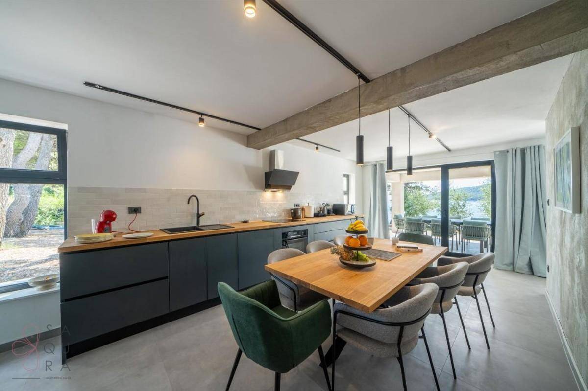 Moderne Küche mit Essbereich, Holzarbeitsplatte und großen Fenstern mit Blick ins Grüne und zum Meer.