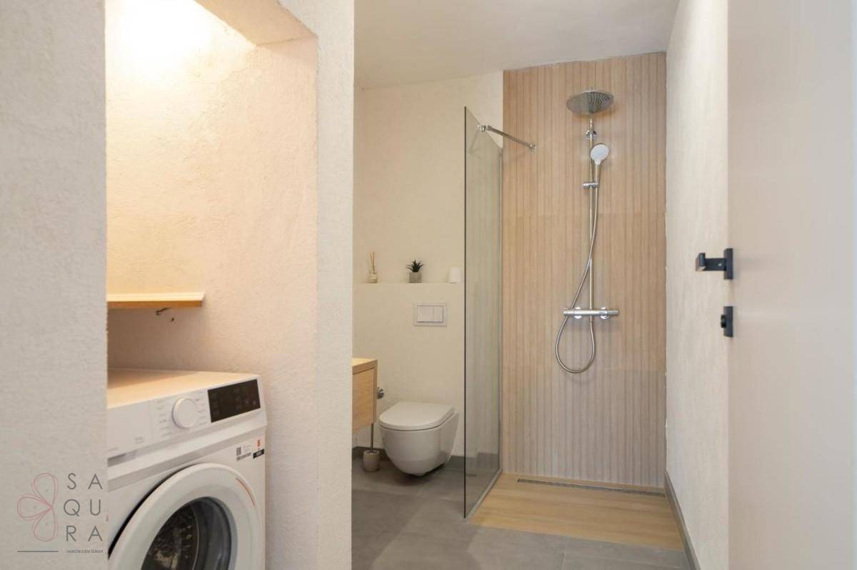 Modernes Badezimmer mit ebenerdiger Dusche, WC und integriertem Waschmaschinenbereich.