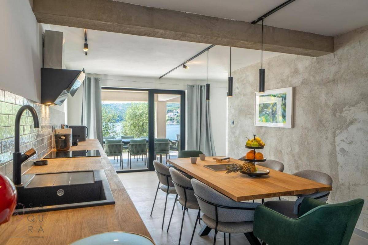 Heller Essbereich mit Holztisch, moderner Küche und direktem Zugang zur Terrasse mit Meerblick.