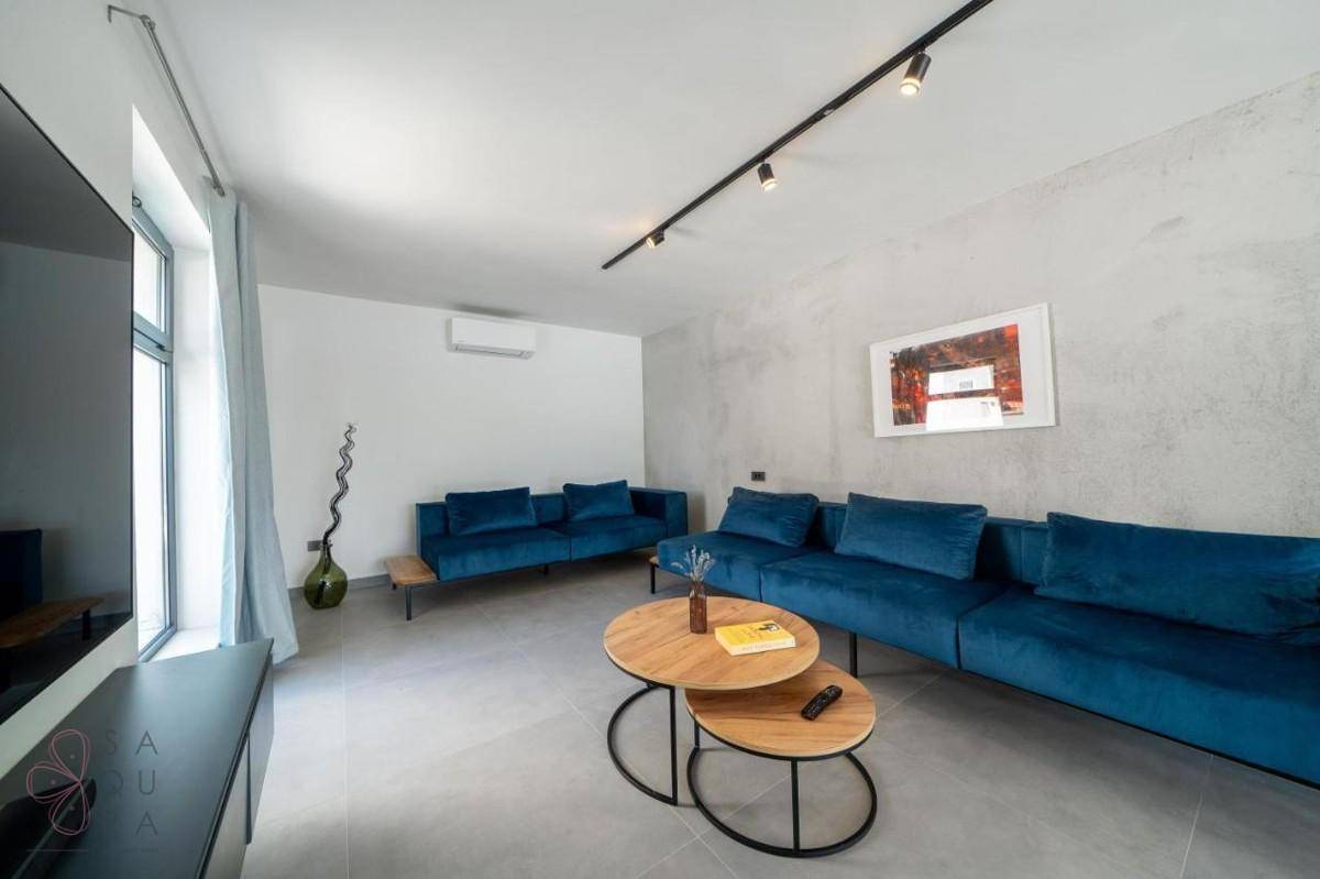 Großzügiges Wohnzimmer mit blauen Sofas, modernen Couchtischen und Klimaanlage.