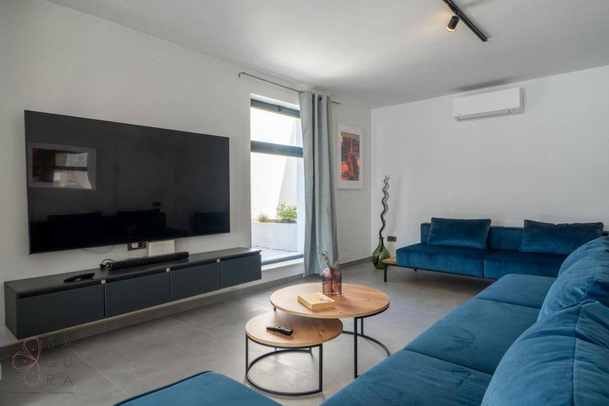 Modernes Wohnzimmer mit großem Fernseher, blauen Sofas und Zugang zu einem Außenbereich.